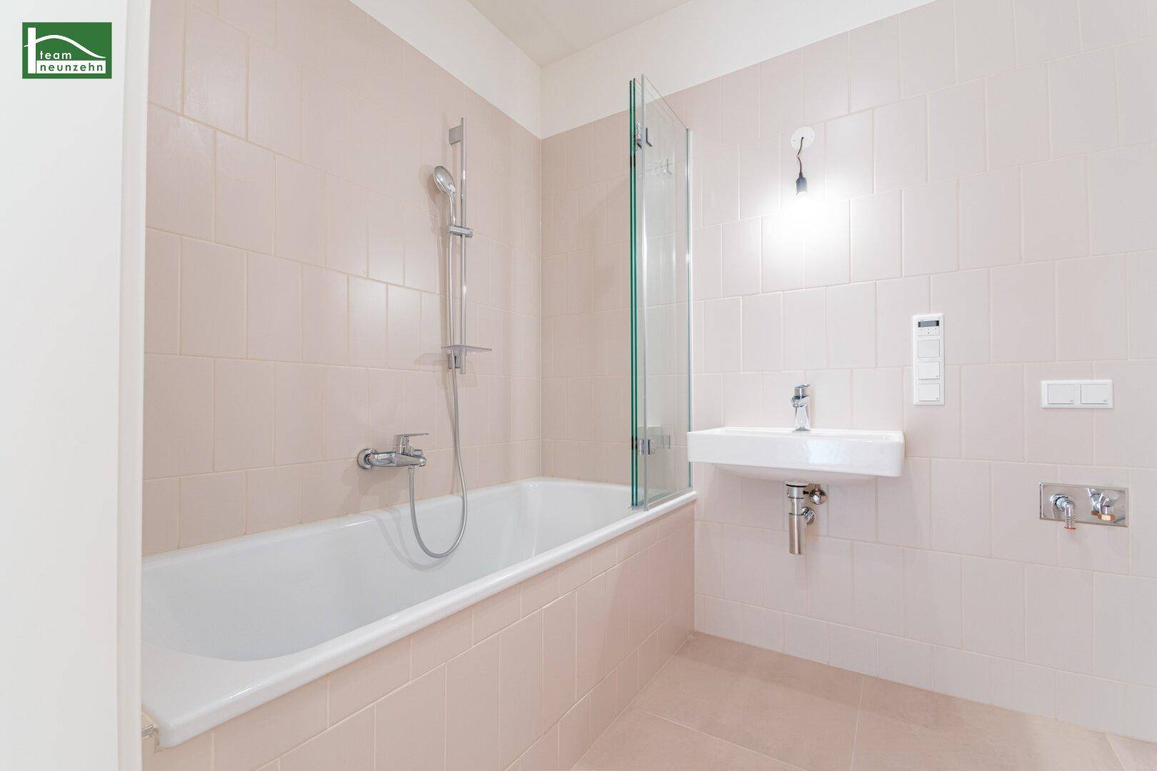 Modernes Badezimmer mit beigefarbenen Fliesen, Badewanne mit Duschwand und einem einzelnen Waschbecken.