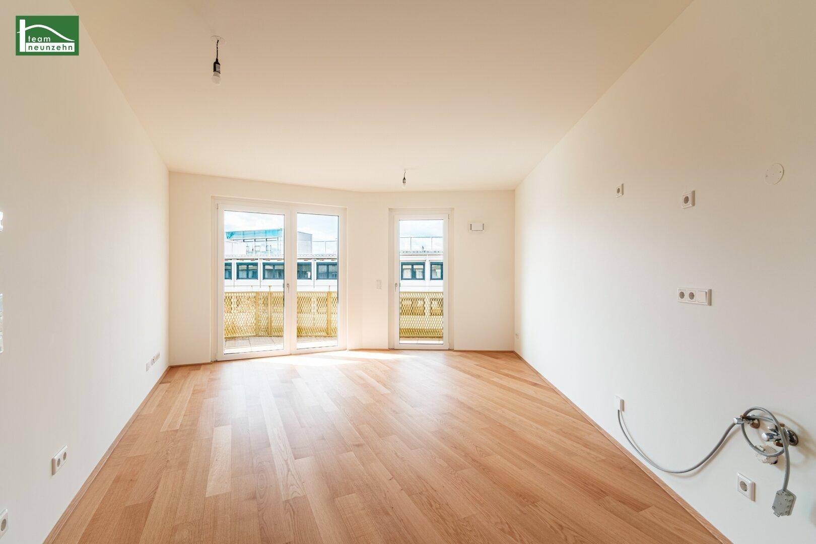 Heller, leerer Raum mit hellem Parkettboden und Zugang zu einem Balkon durch große Glastüren.