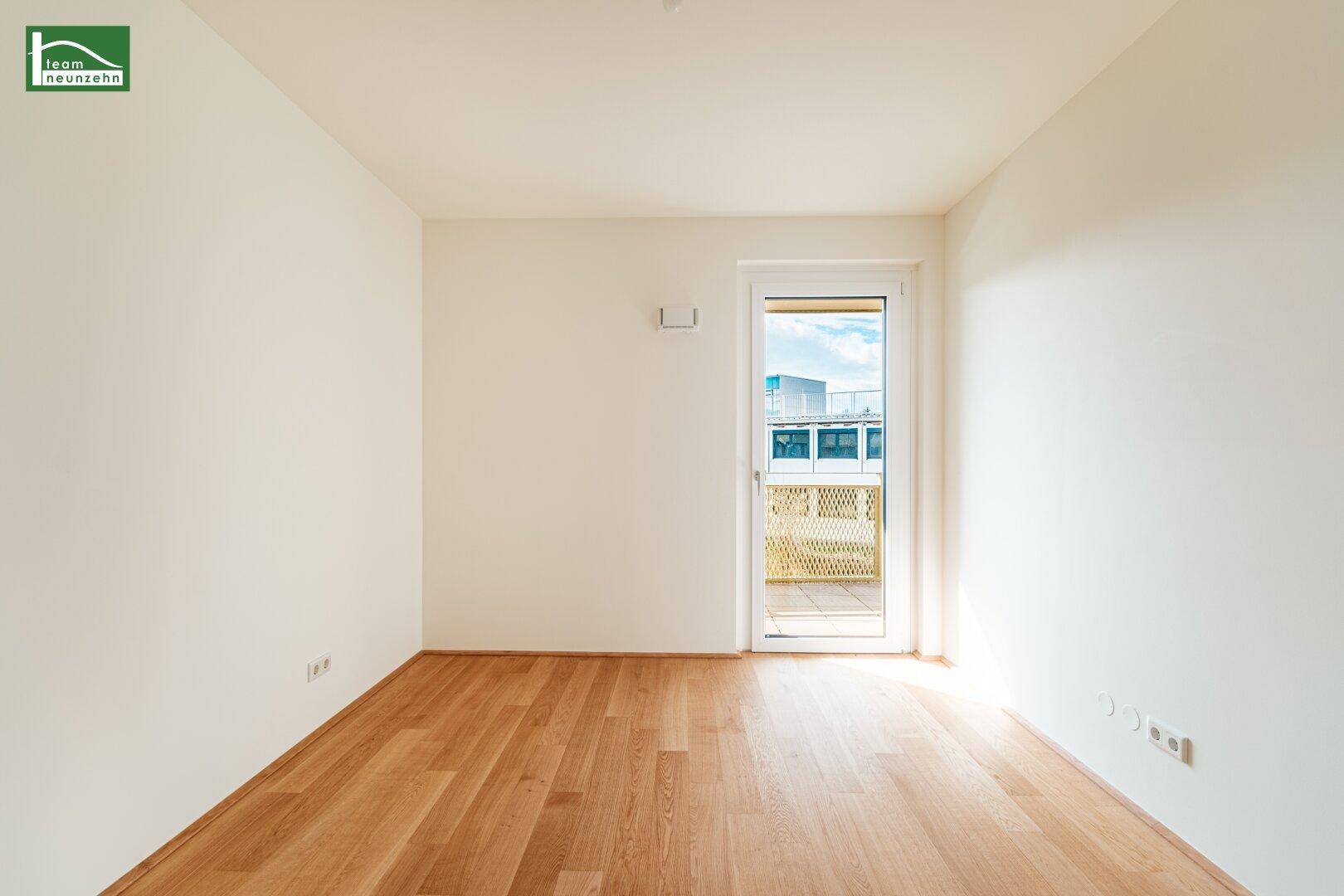 Schlafzimmer mit hellem Parkettboden, weißen Wänden und direktem Zugang zu einem kleinen Balkon.