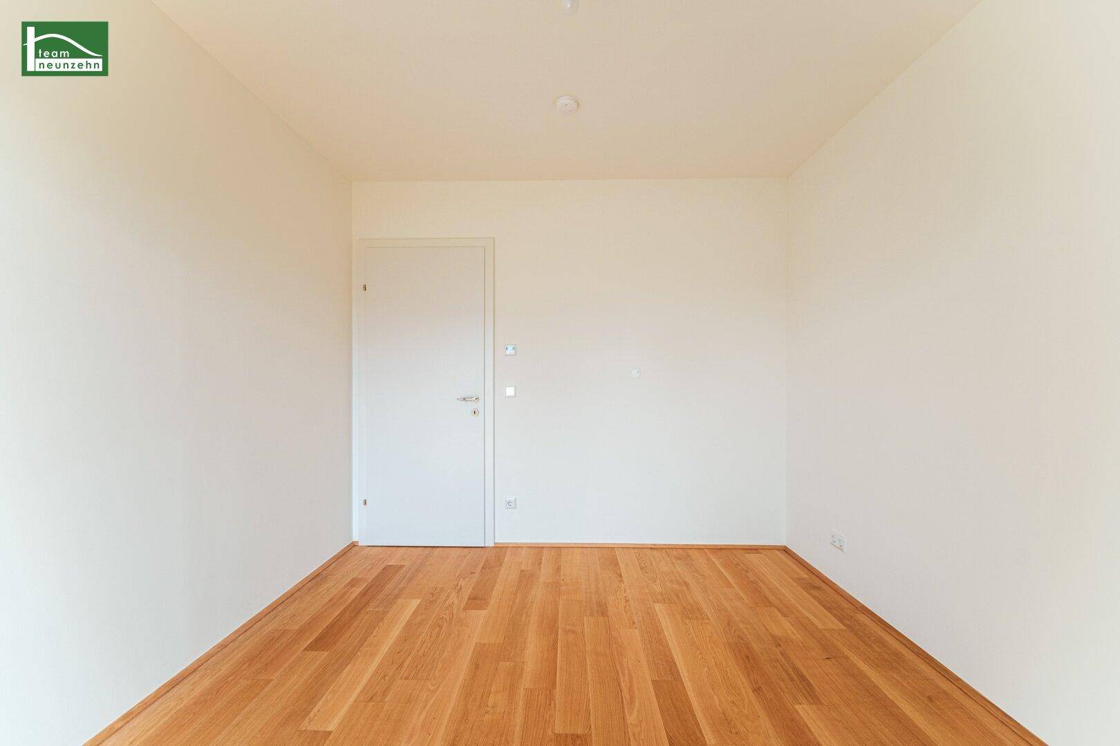 Leeres Zimmer mit hellem Parkettboden und weißer Tür, ideal als Schlaf- oder Arbeitszimmer.