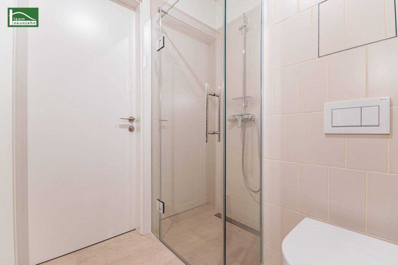 Duschbereich im modernen Badezimmer mit Glasabtrennung und beigefarbenen Fliesen.