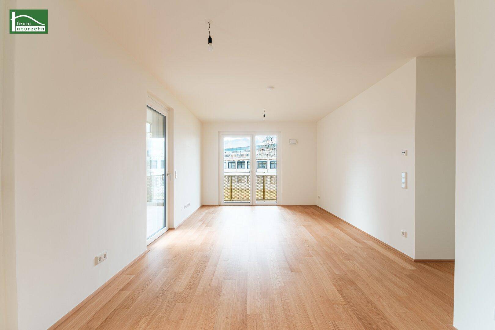 Helles, leeres Wohnzimmer mit Parkettboden und Zugang zum Balkon.