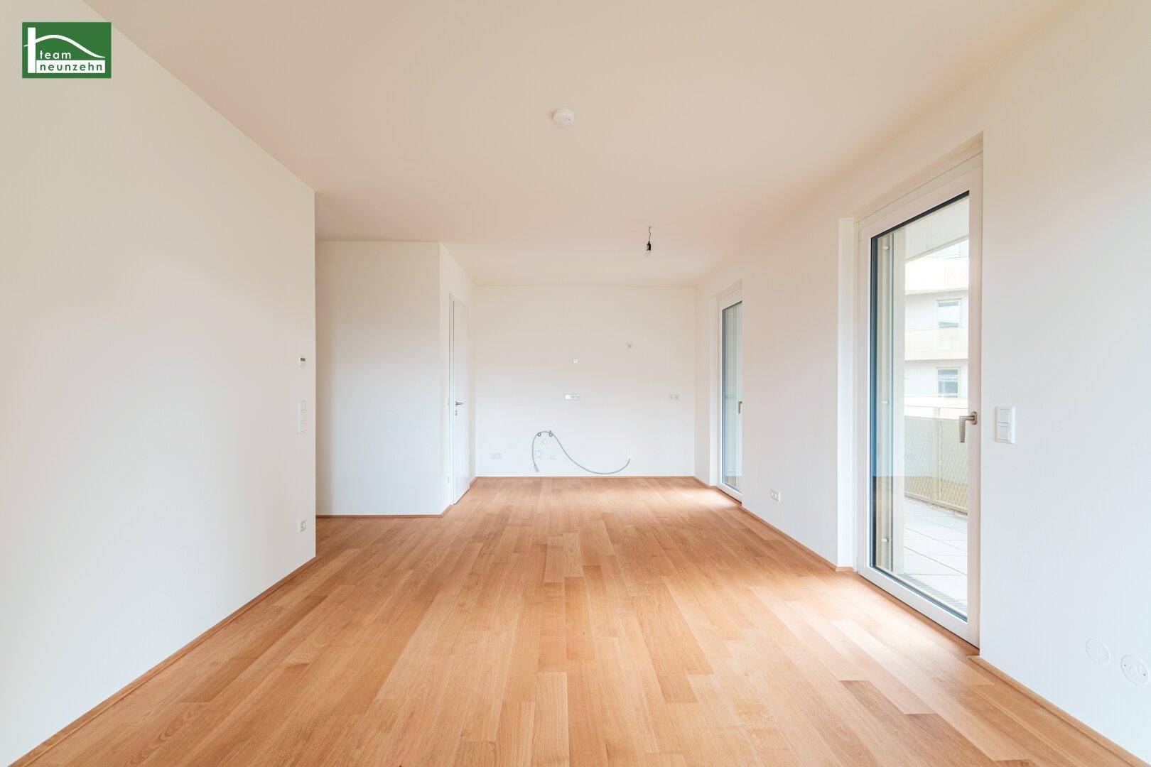 Lichtdurchfluteter Raum mit Holzboden und Zugang zu einem Außenbereich.