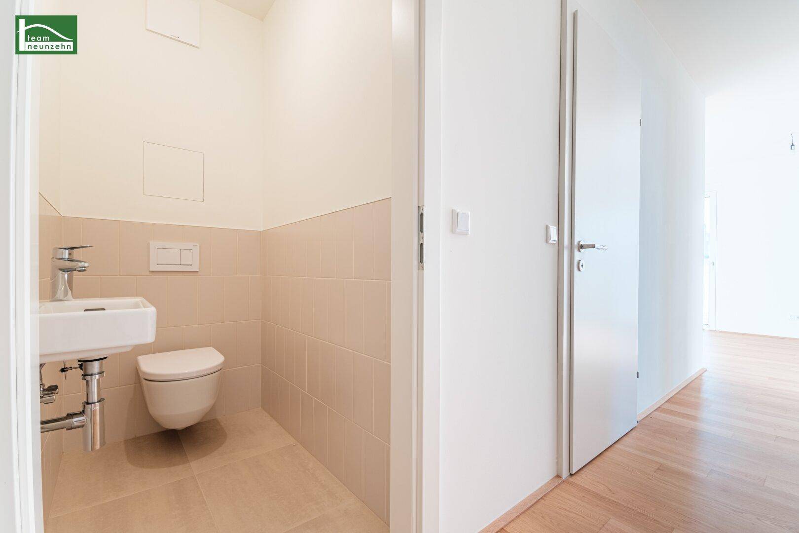 Gäste-WC mit wandhängendem WC, kleinem Waschbecken und hellen Fliesen.