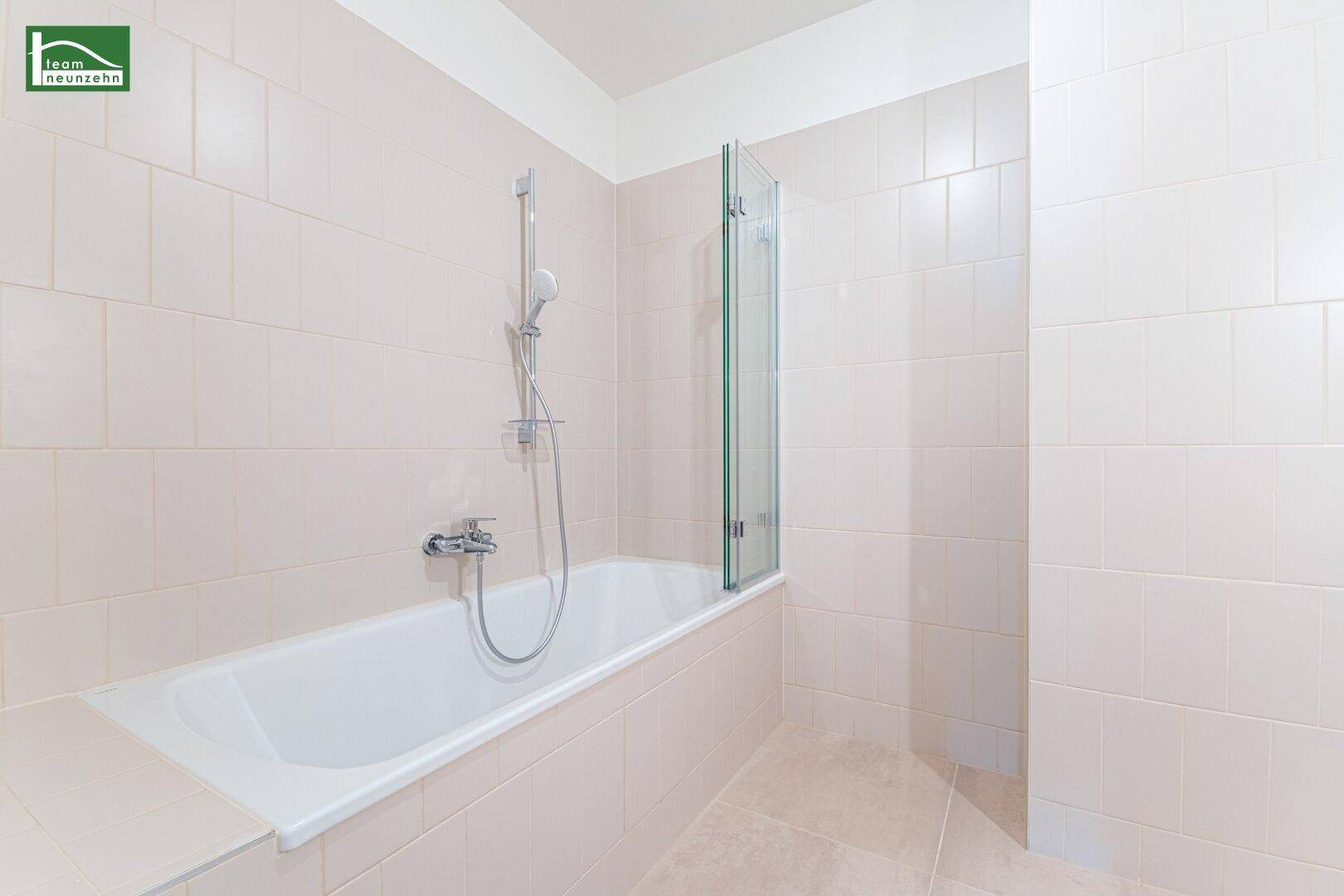 Modernes Badezimmer mit Badewanne, Duschwand und hellen Fliesen.
