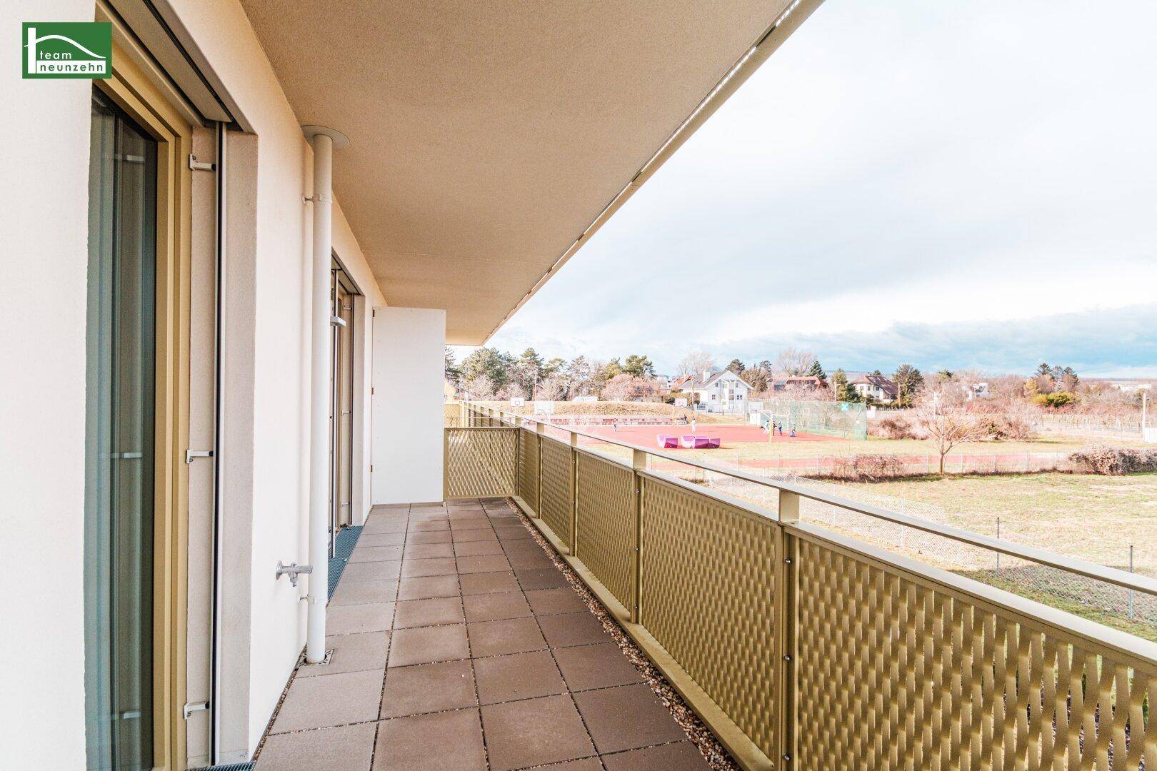 Geräumiger Balkon mit Fliesenboden und Metallgeländer, bietet weiten Blick ins Grüne.