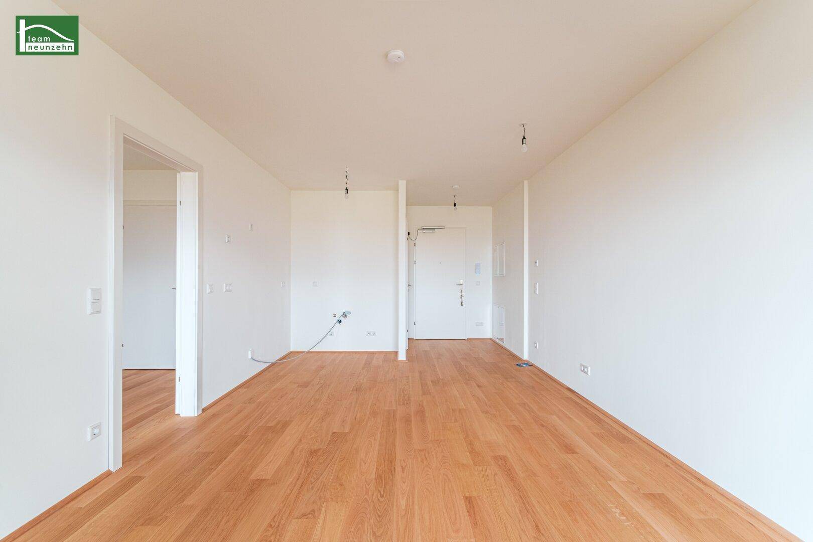 Geräumiger, unmöblierter Raum mit Holzfußboden und weißen Wänden, bereit zum Einzug.
