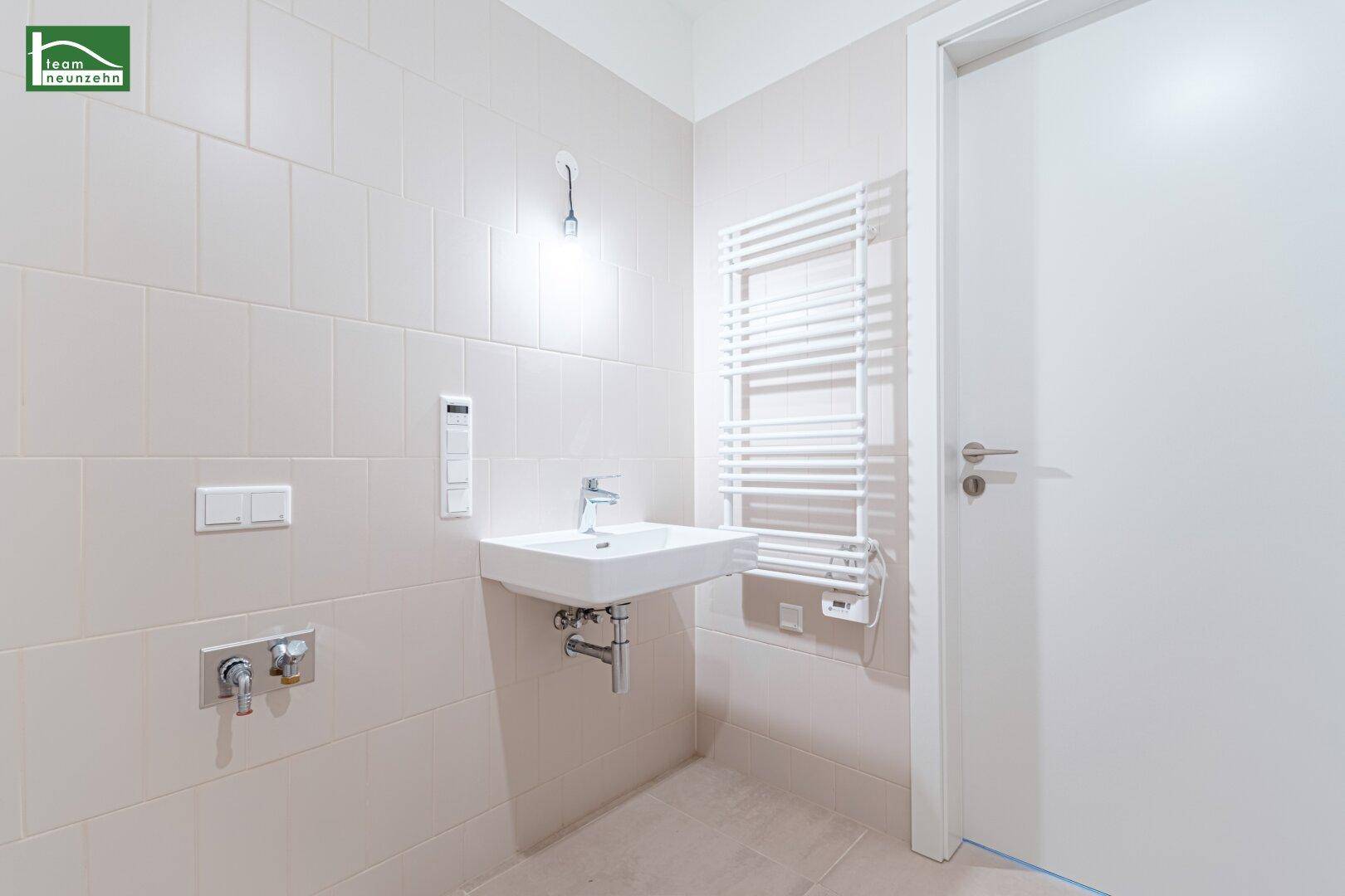 Modernes Badezimmer mit beigefarbenen Fliesen, wandhängendem Waschbecken und Handtuchheizkörper.