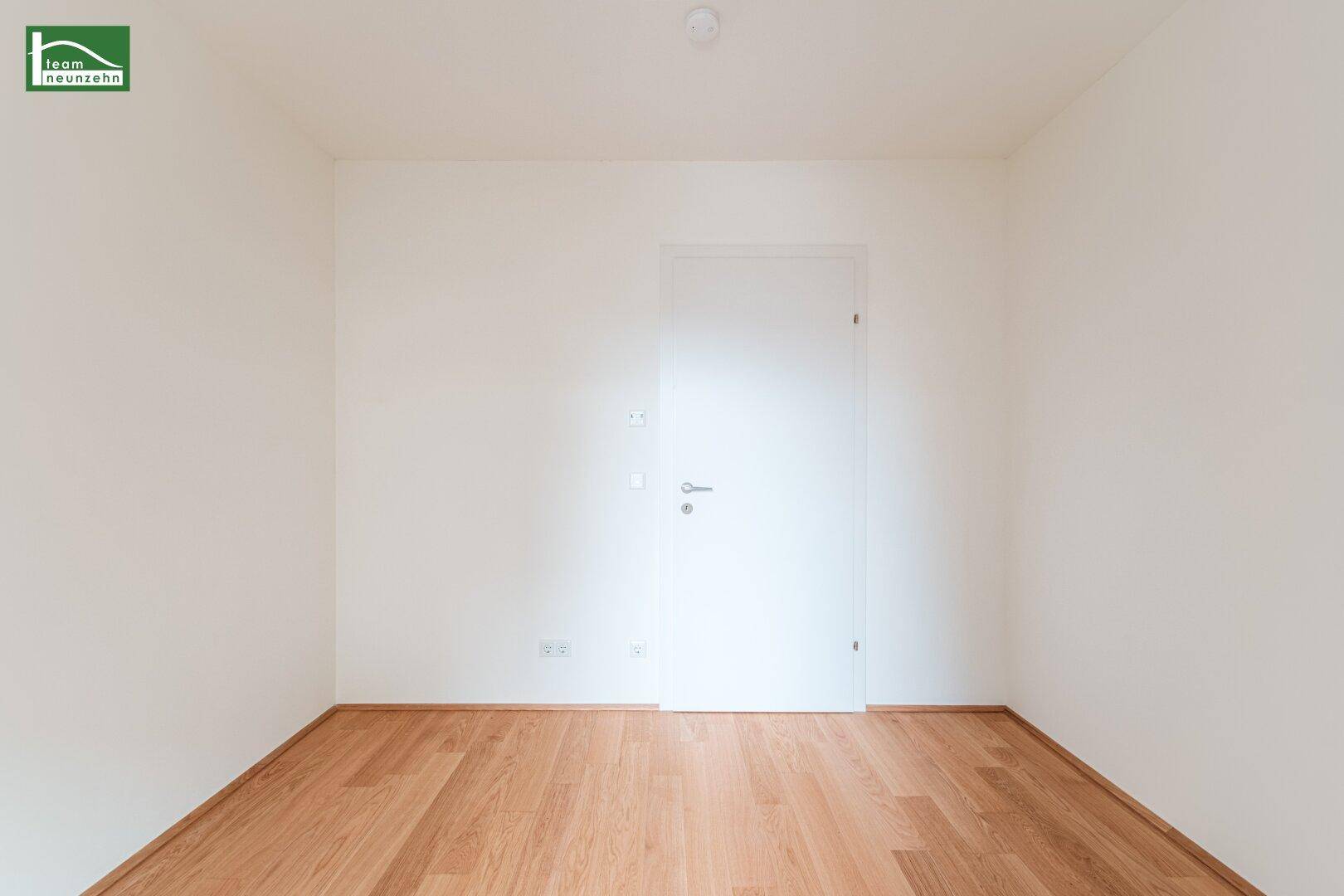 Neutrales Zimmer mit hellem Holzparkett und weißen Wänden, ideal als Schlaf- oder Arbeitszimmer.