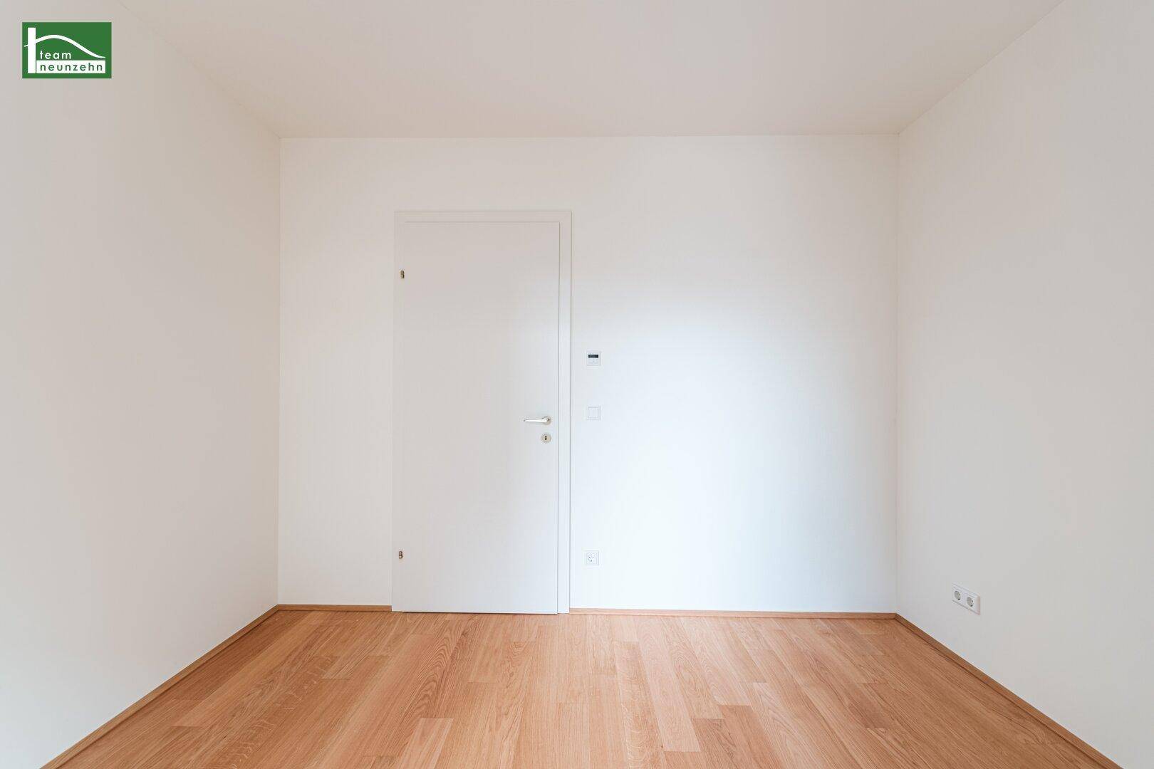 Schlichtes Zimmer mit hellem Holzparkett und weißen Wänden, bereit für individuelle Gestaltung.