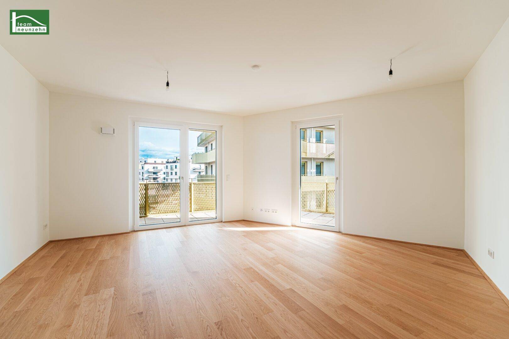 Heller, leerer Wohnraum mit hellem Parkettboden und Zugang zu einem Balkon.