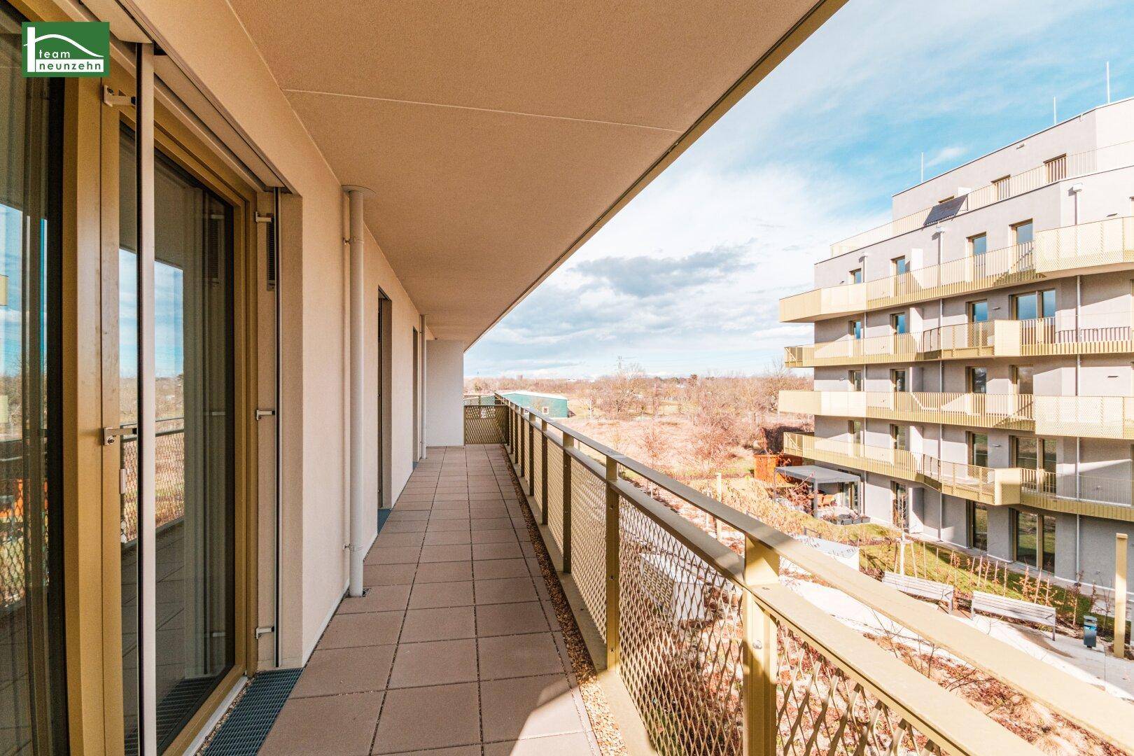 Ausgedehnter Balkon mit Fliesen und Blick auf die grüne Umgebung und weitere Gebäude.