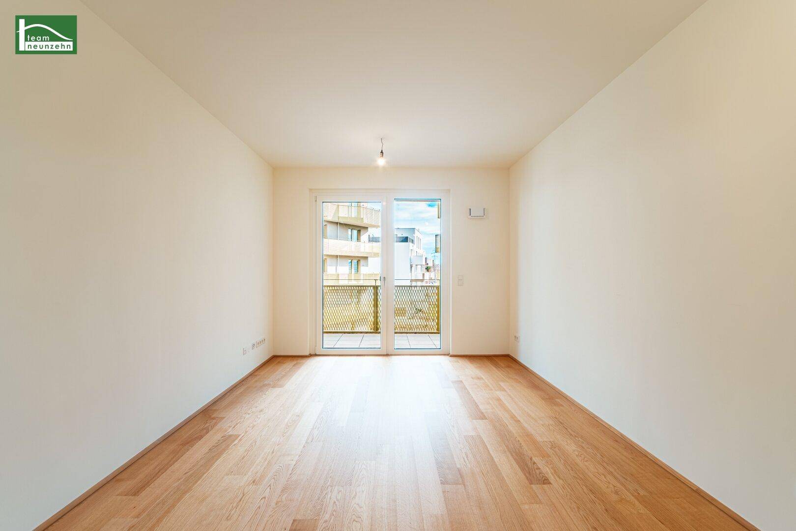 Heller, leerer Raum mit Holzboden und Zugang zu einem Balkon.