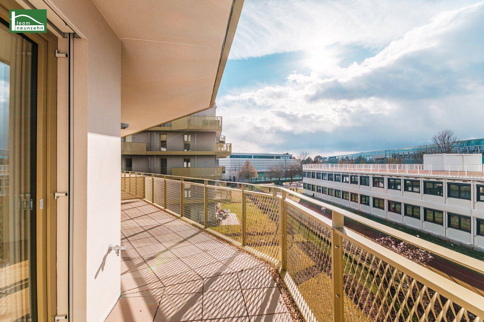 Sonniger Balkon mit Blick auf die umliegende Grünfläche und moderne Gebäude.