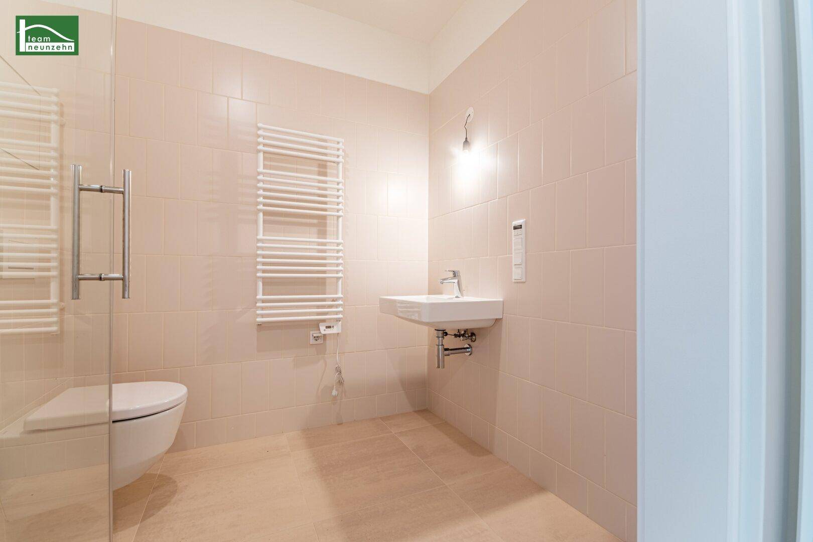 Helles Badezimmer mit modernem Waschbecken, beheiztem Handtuchhalter und beigefarbenen Fliesen.