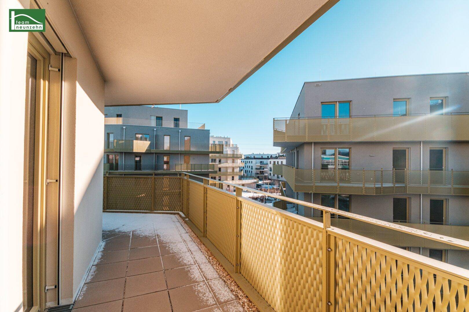 Heller Balkon mit Fliesenboden und Blick auf die moderne Wohnanlage im Winter.