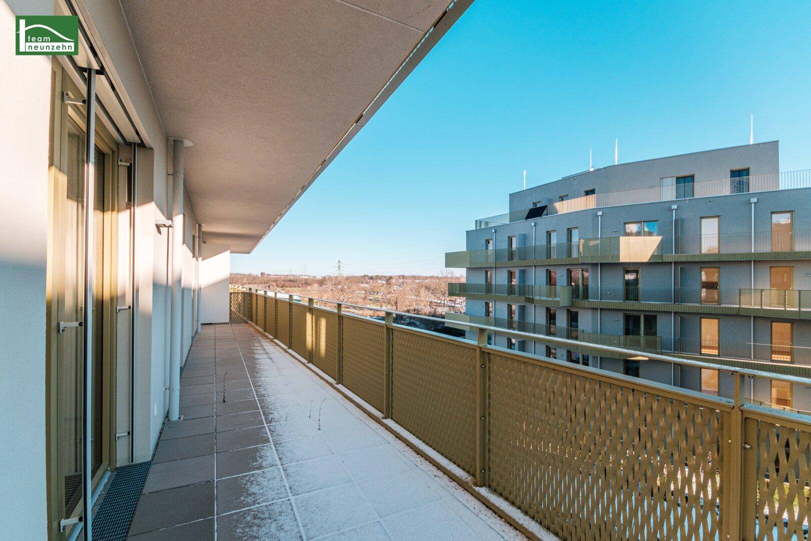 Langer Balkon mit Fliesenboden und modernem Geländer, bietet weite Aussicht über die Umgebung.
