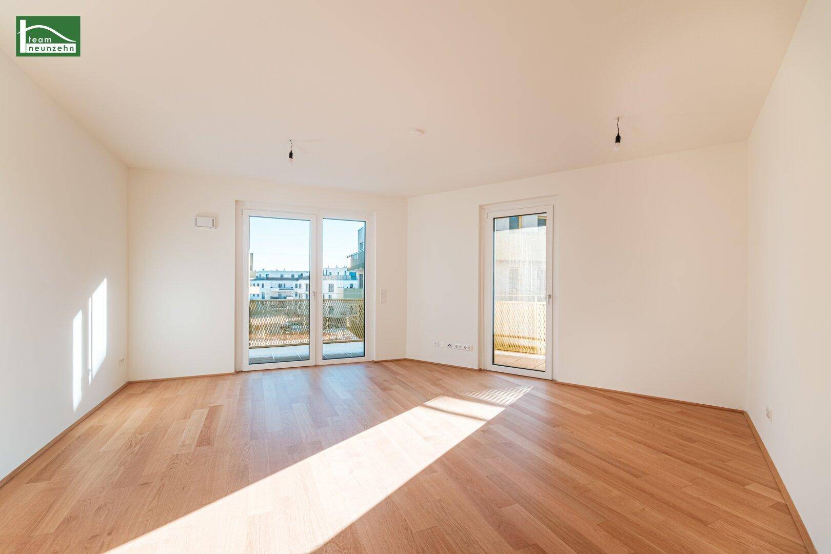 Lichtdurchflutetes Wohnzimmer mit hellem Parkettboden und Zugang zum Balkon.