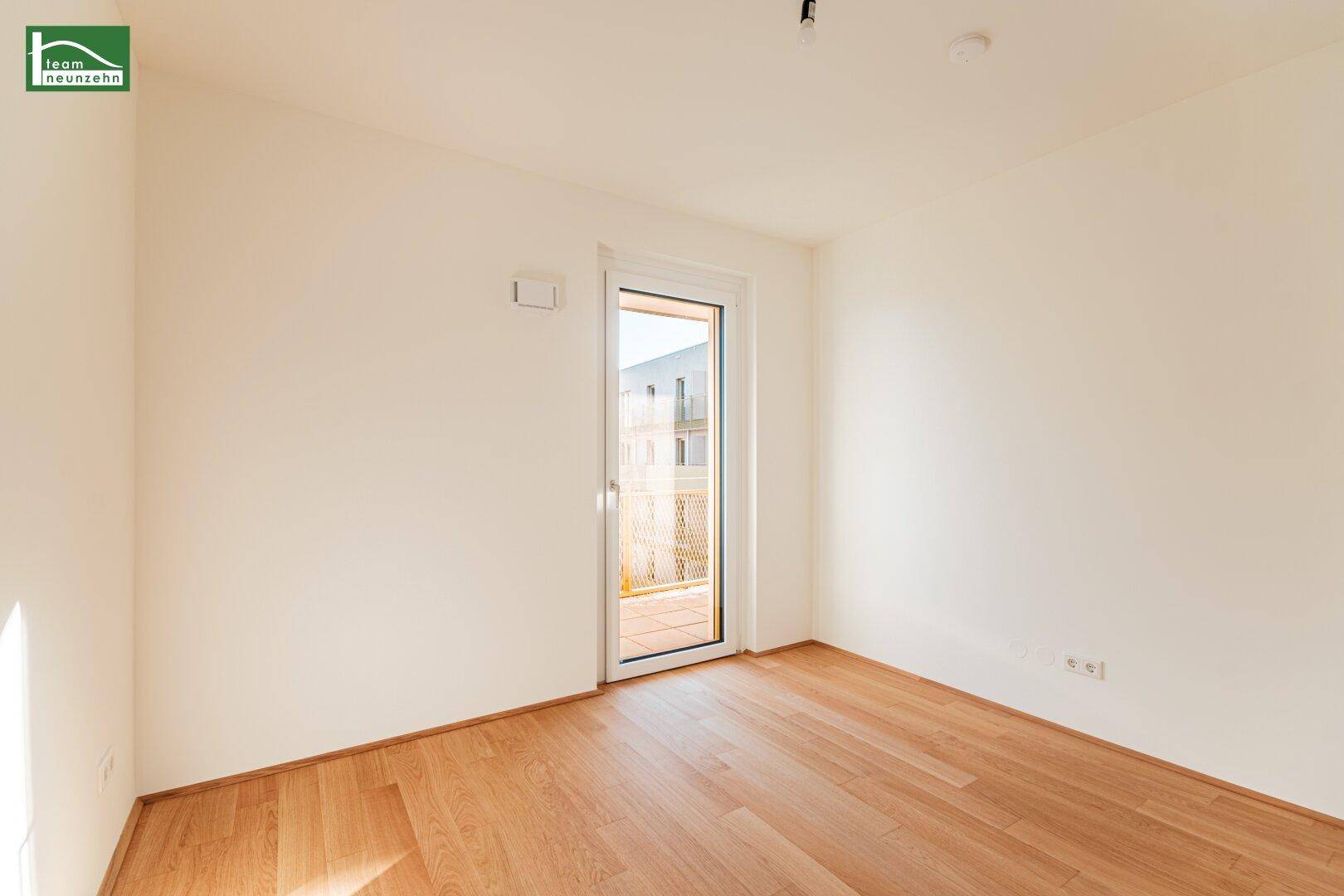 Lichtdurchflutetes Zimmer mit Holzboden und Zugang zu einem Balkon, ideal für ein Schlafzimmer.