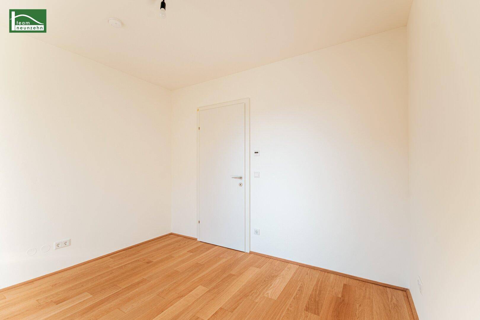 Neutral gestaltetes Zimmer mit Holzboden und weißer Tür, vielseitig nutzbar.