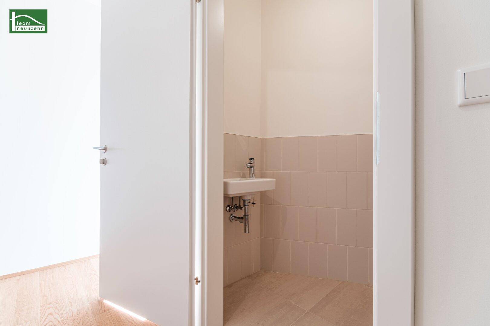 Kleines Gäste-WC mit Waschbecken und hellen Fliesen, praktisch und funktional gestaltet.