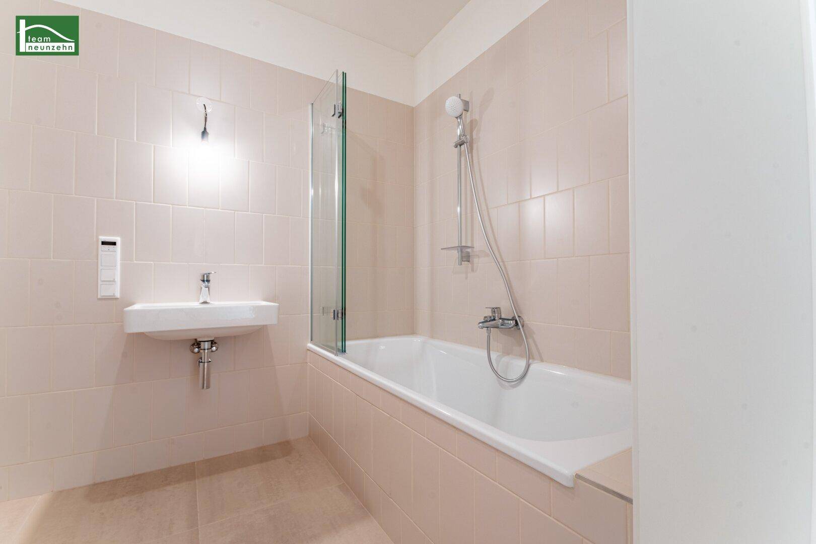 Modernes Badezimmer mit Badewanne, Waschbecken und hellen Fliesen an Wänden und Boden.