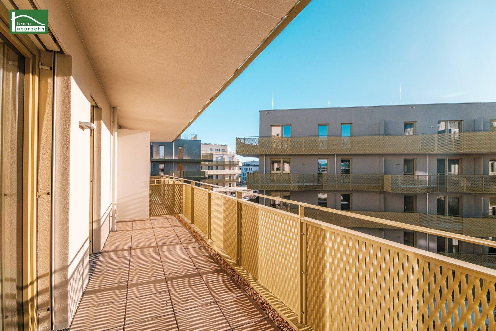 Langer Balkon mit geländer und Blick auf die umliegenden Neubauten bei Sonnenschein.