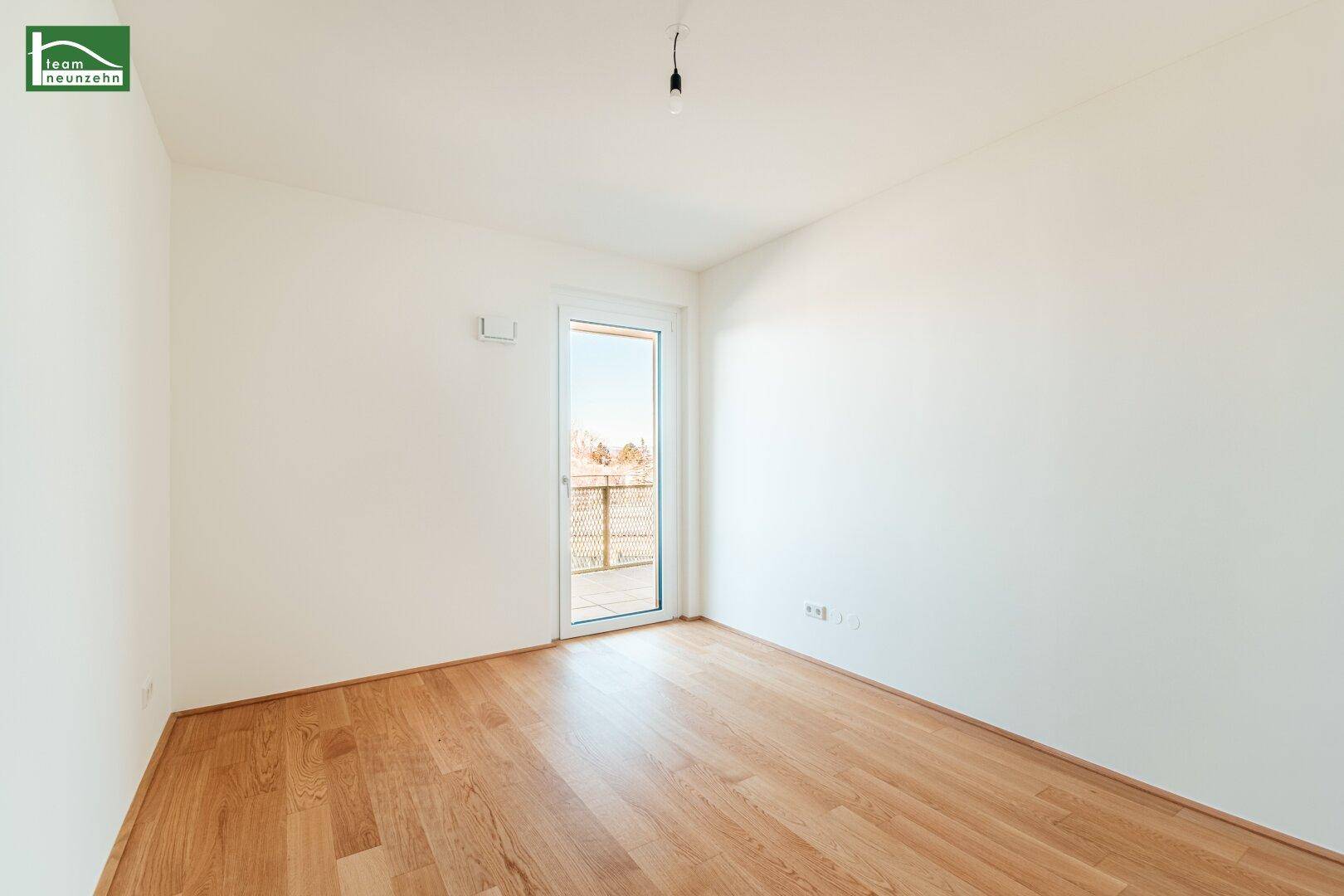 Helles Schlafzimmer mit Parkettboden und Zugang zu einem französischen Balkon.