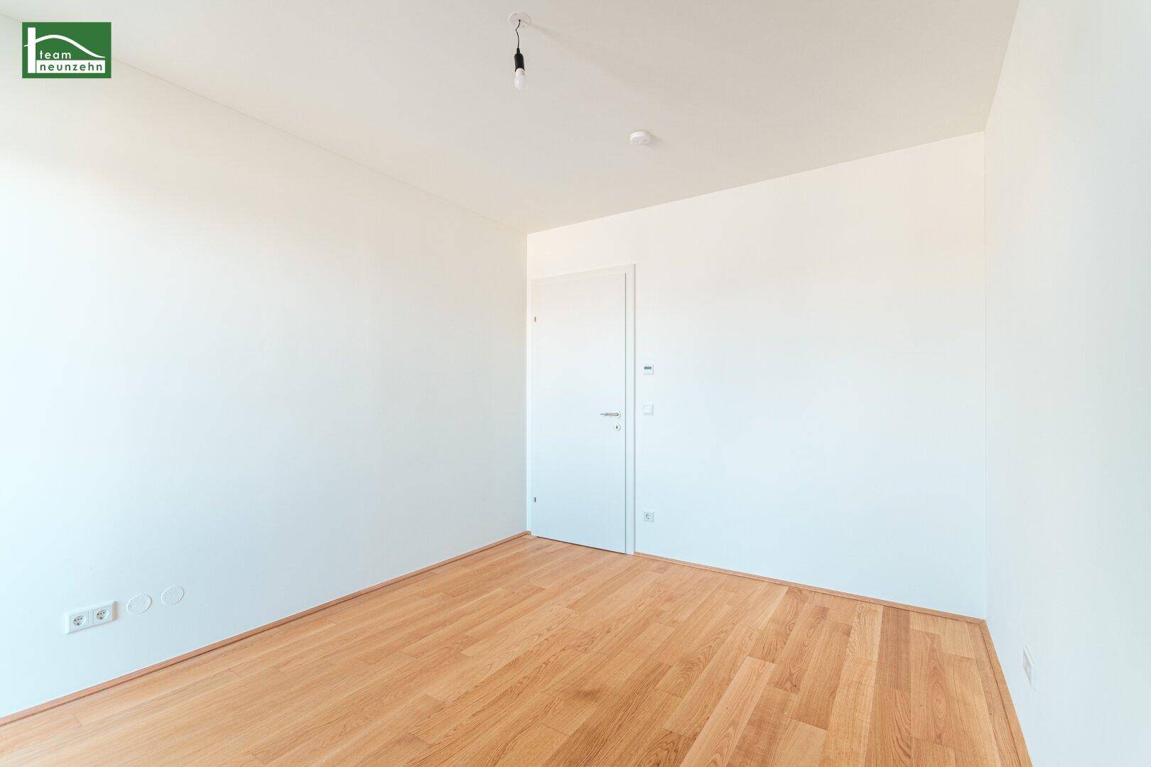 Unmöbliertes Zimmer mit hellem Holzboden und weißer Tür, ideal als Schlafzimmer.
