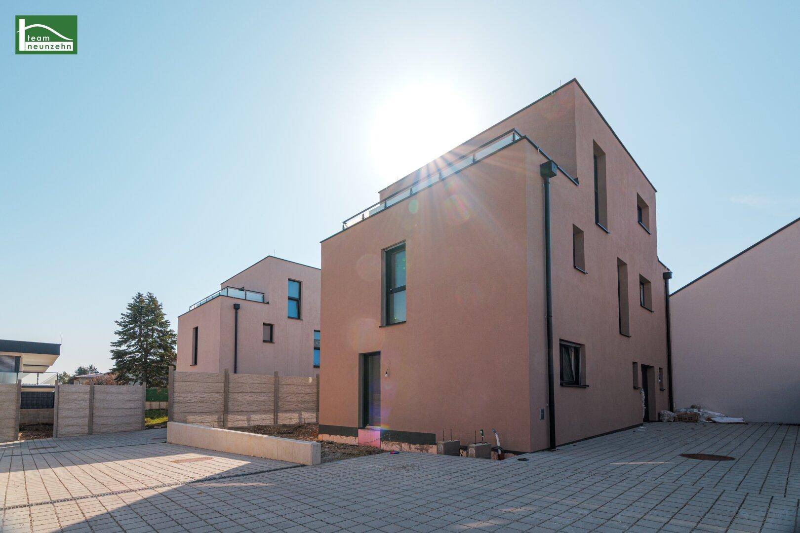 Moderne Neubau-Doppelhaushälfte mit klaren Linien und gepflastertem Vorplatz unter strahlendem Himmel.