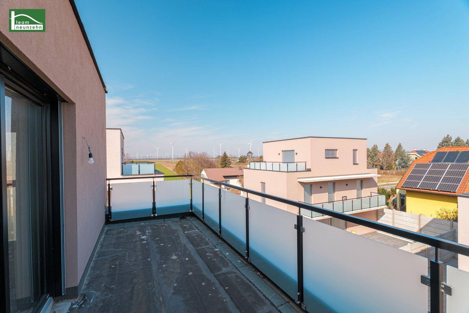 Großer Balkon mit Glasgeländer und weitem Blick über die Landschaft mit Windrädern.
