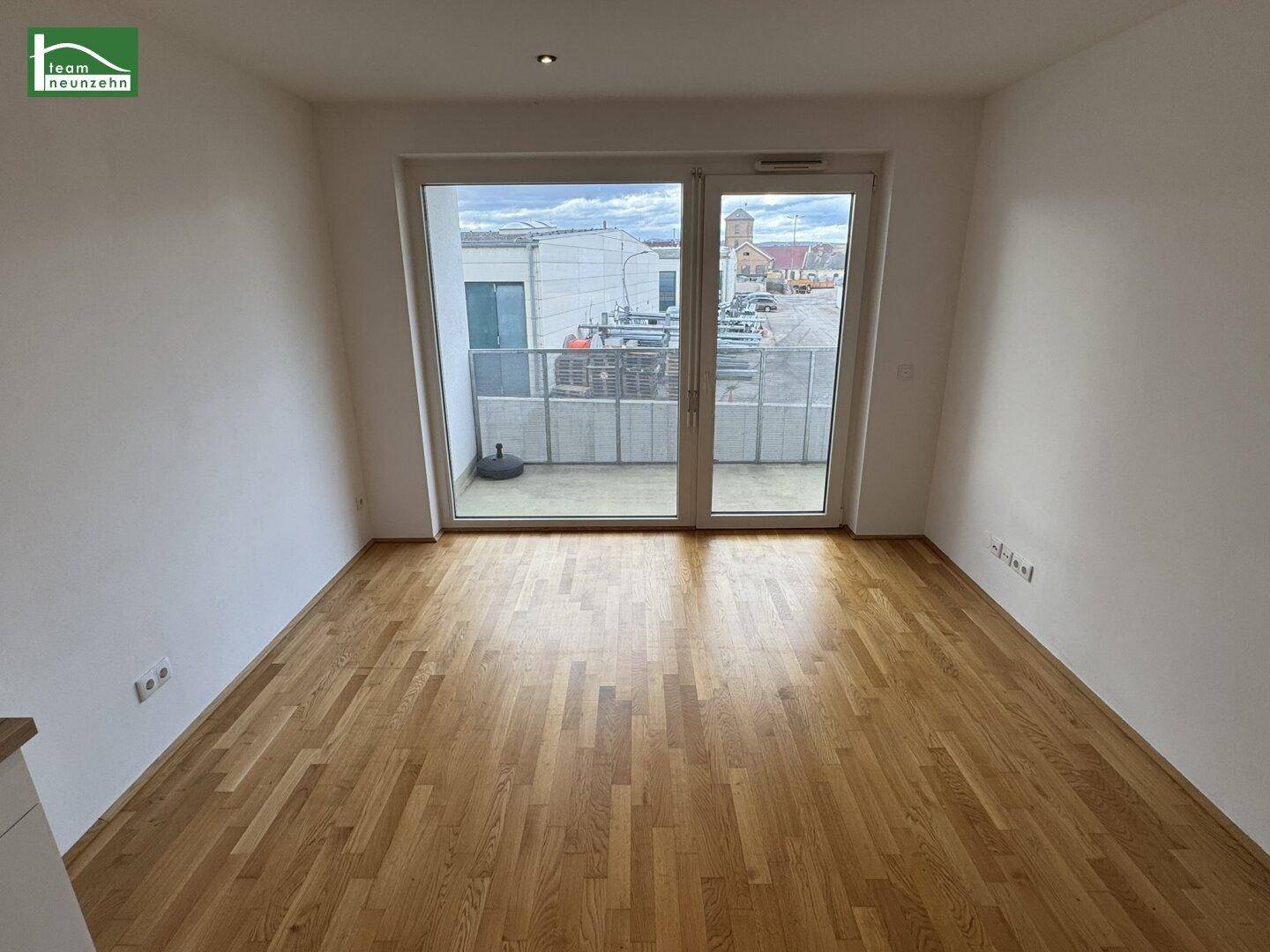 Geräumiger, heller Raum mit Parkettboden und großen Fenstern, die auf einen Balkon führen.