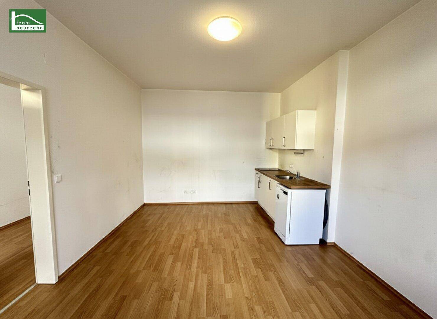 Geräumiger Wohnbereich mit Laminatboden und einer kleinen, funktionalen Küchenzeile.