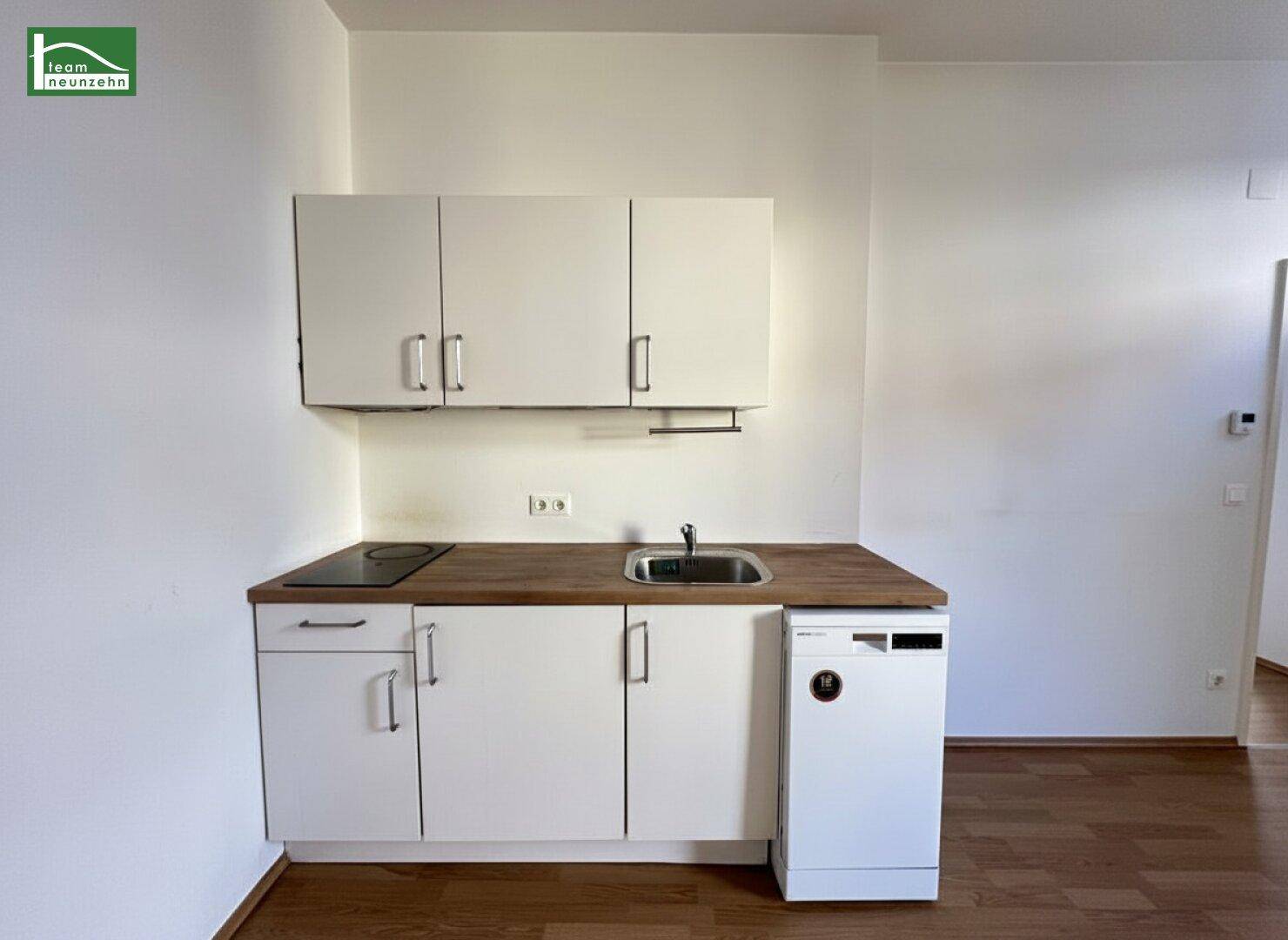 Funktionale Küchenzeile mit weißen Schränken, Holz-Arbeitsplatte und integriertem Geschirrspüler.