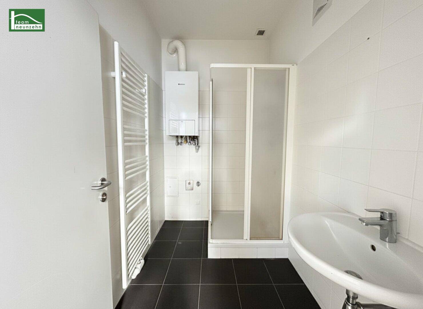 Modernes Badezimmer mit Dusche, Waschbecken, Handtuchheizkörper und dunklen Fliesen.