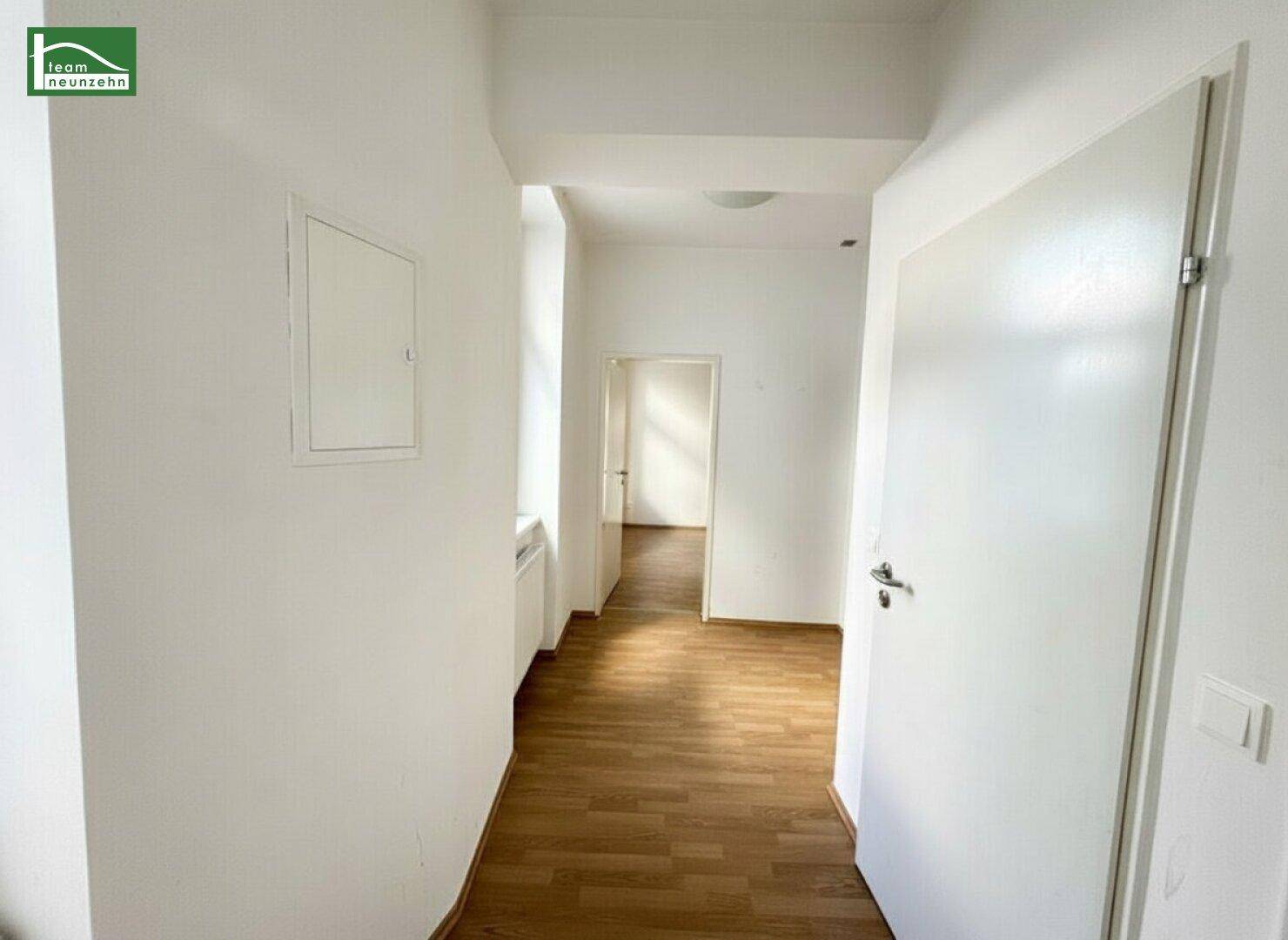Heller Flur mit Laminatboden, weißen Wänden und Zugang zu weiteren Räumen.