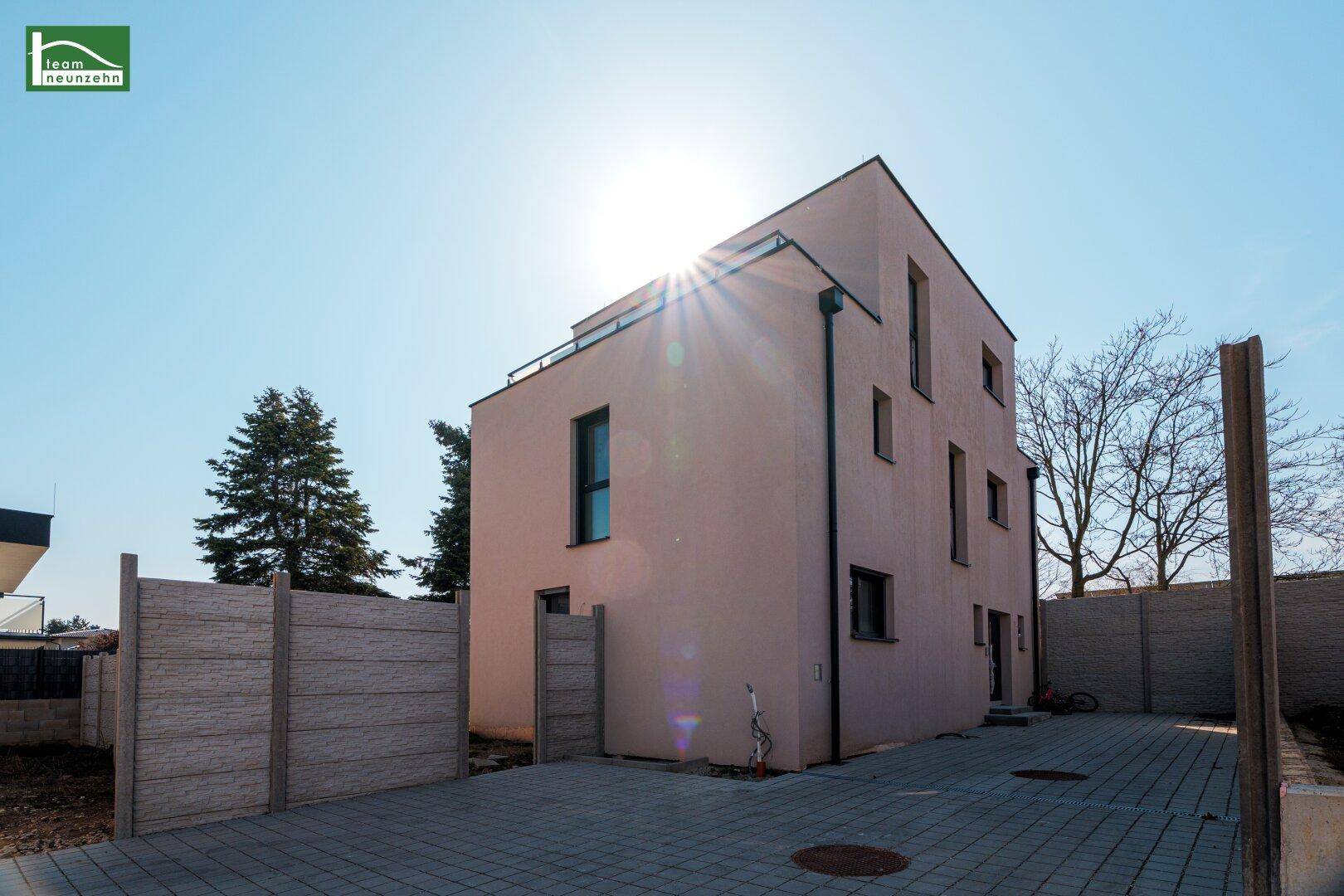 Rückansicht des modernen Hauses mit gepflasterter Auffahrt und sonnigem Außenbereich.