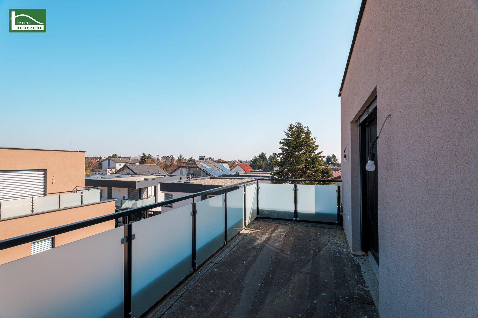 Geräumiger Balkon mit Glasgeländer und Blick auf die umliegende Wohngegend.
