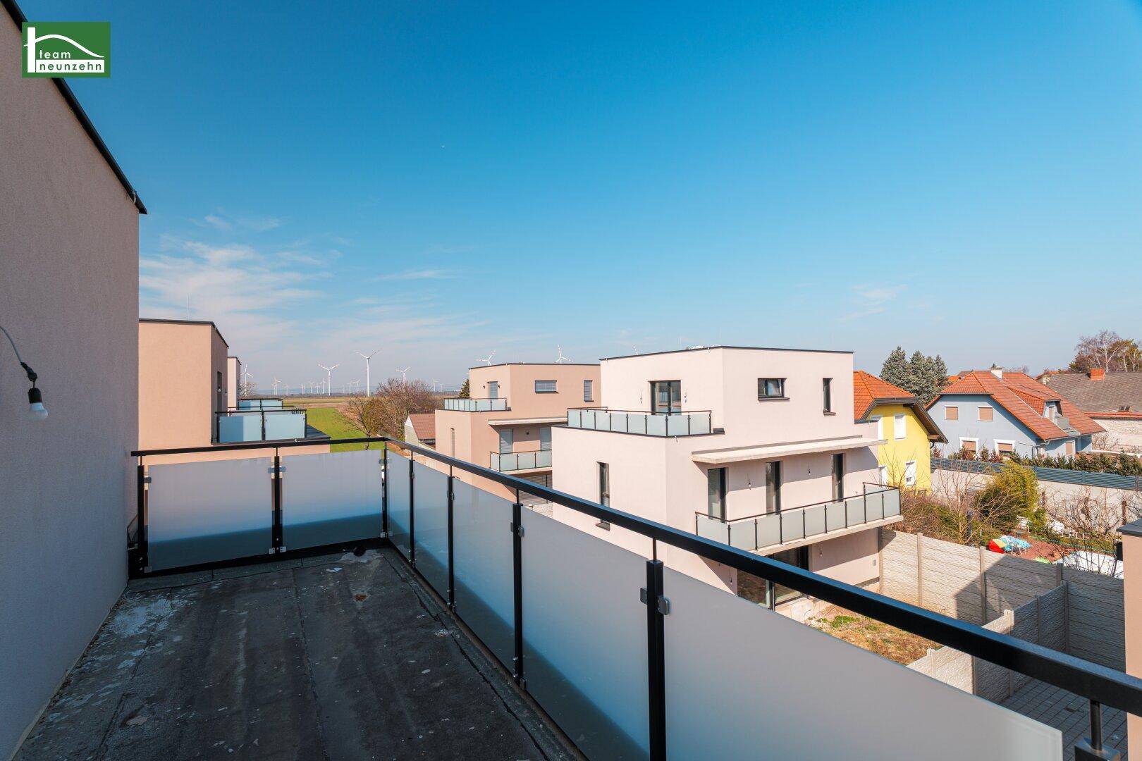 Balkon mit moderner Glasbrüstung und weitem Blick über die Nachbarschaft und Landschaft.