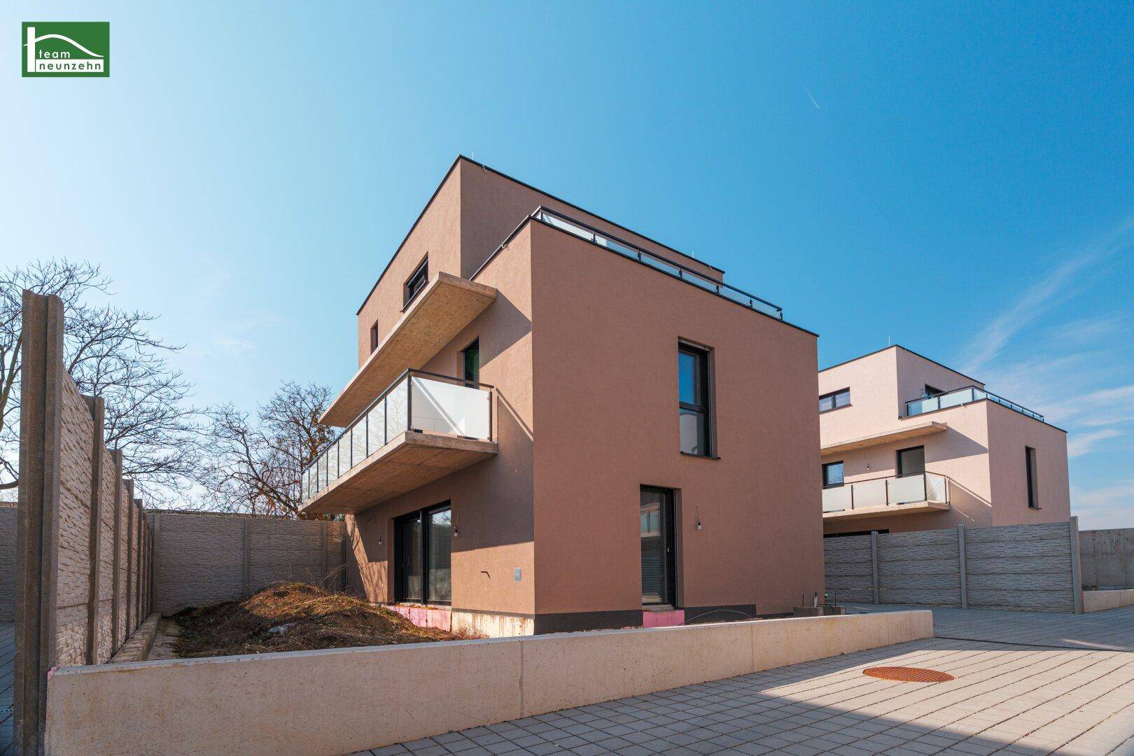 Neubau-Reihenhäuser mit modernen Balkonen und heller Fassade in sonniger Umgebung.