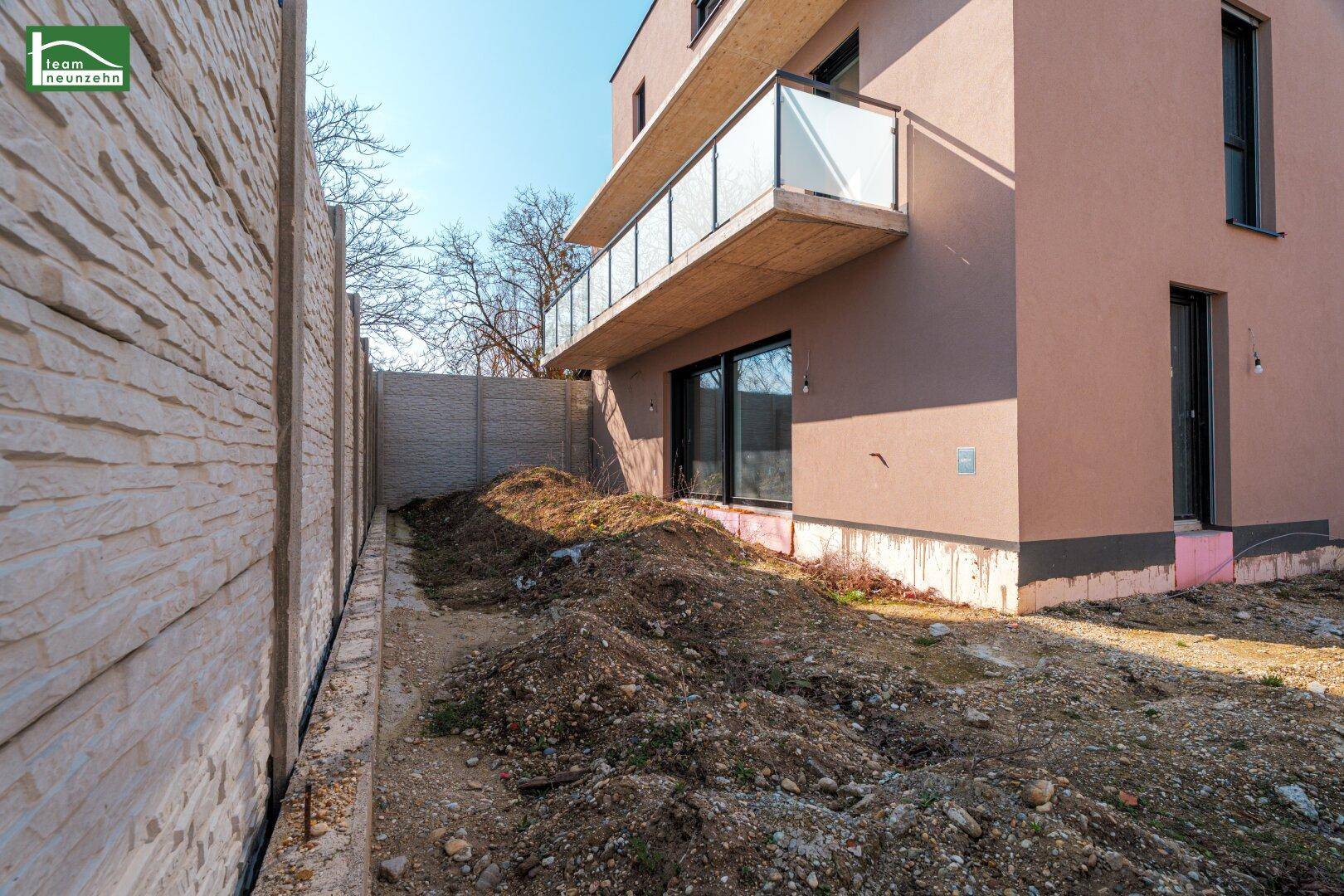 Unfertiger Gartenbereich neben dem Neubau mit Betonzaun und Balkon im Hintergrund.