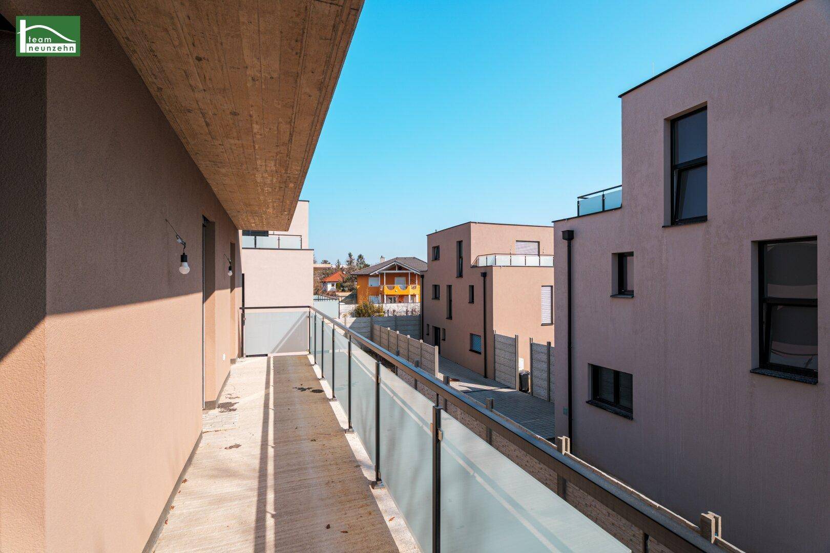 Langer Balkon mit Glasgeländer und Blick auf die umliegenden Neubauten in der Siedlung.