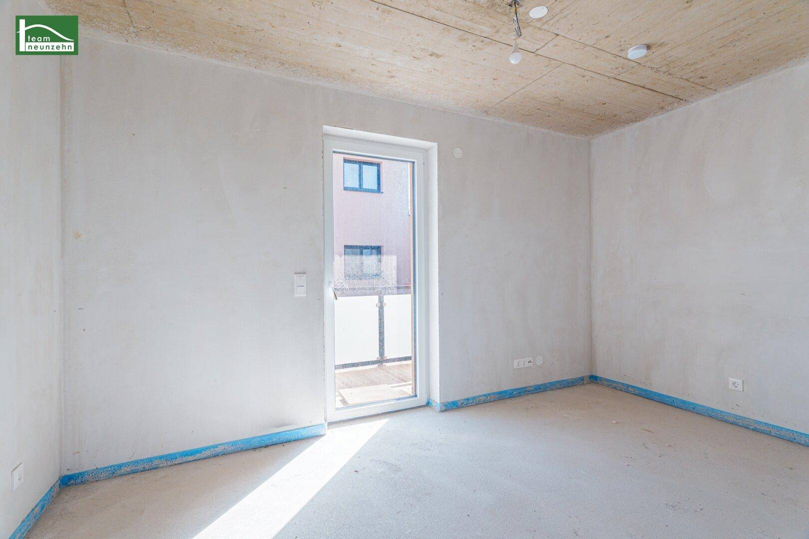 Unfertiger Raum mit Tür zum Balkon und Rohbetondecke, bereit für den Innenausbau.
