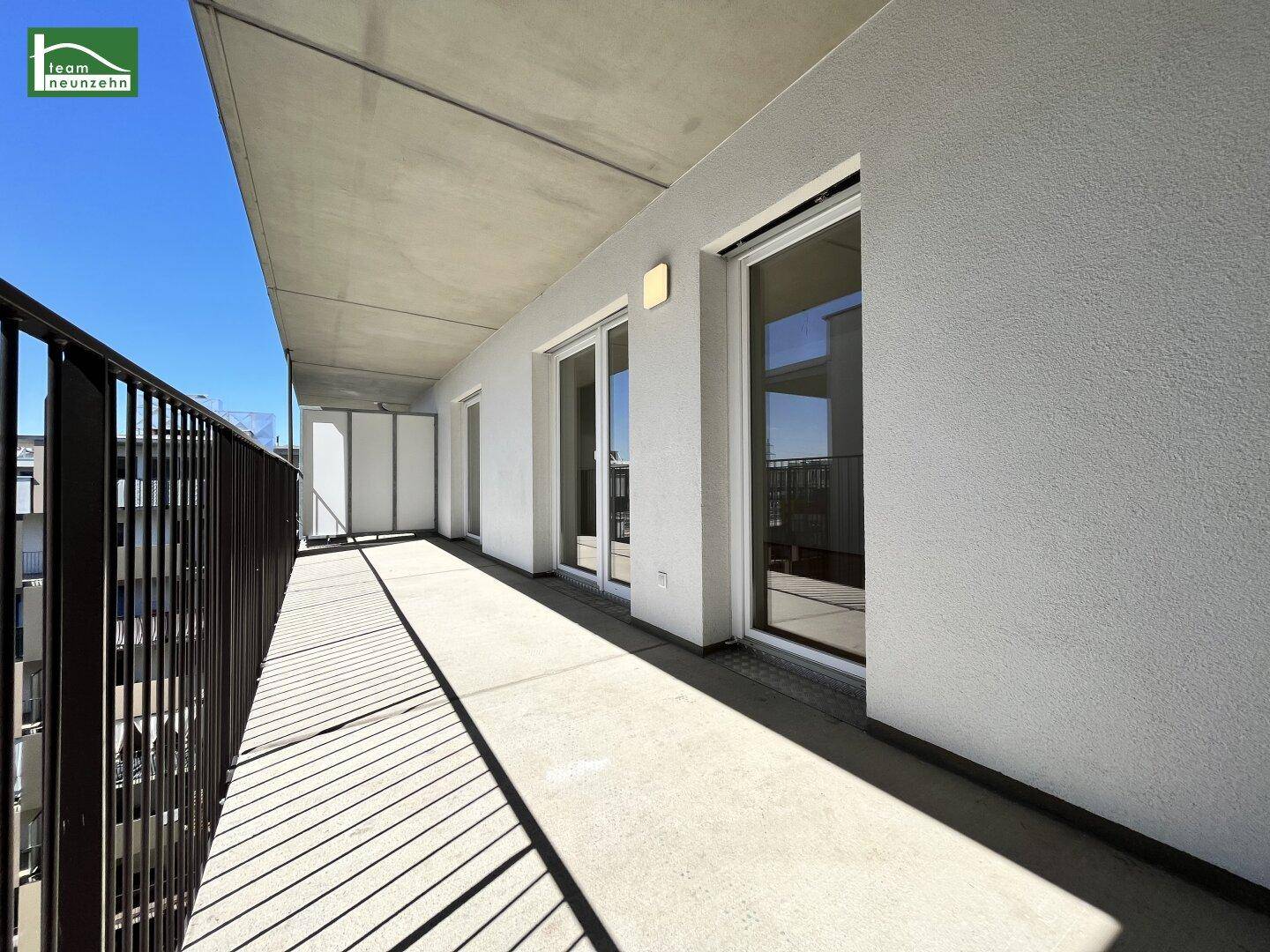 Langer, sonniger Balkon mit Metallgeländer und Blick auf die Umgebung.