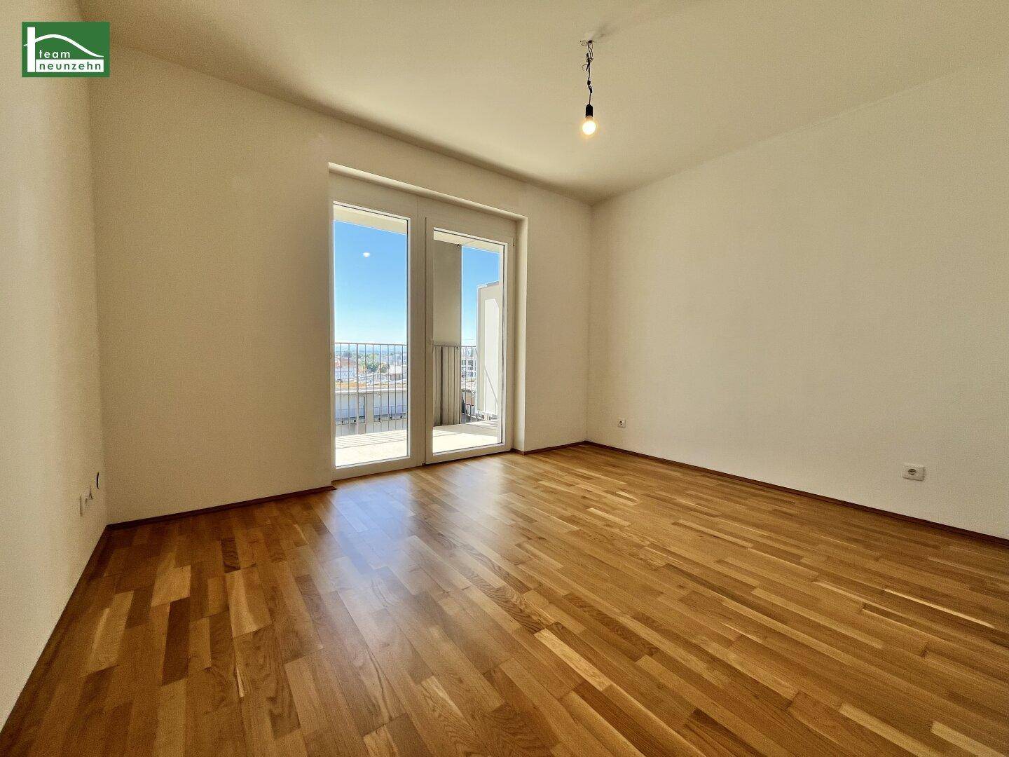Geräumiges Schlafzimmer mit Parkettboden und großem Fenster, das Zugang zu einem Balkon bietet.