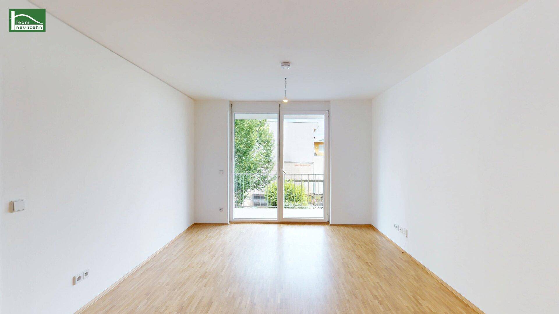 Heller, leerer Raum mit Holzfußboden und Zugang zu einem französischen Balkon.