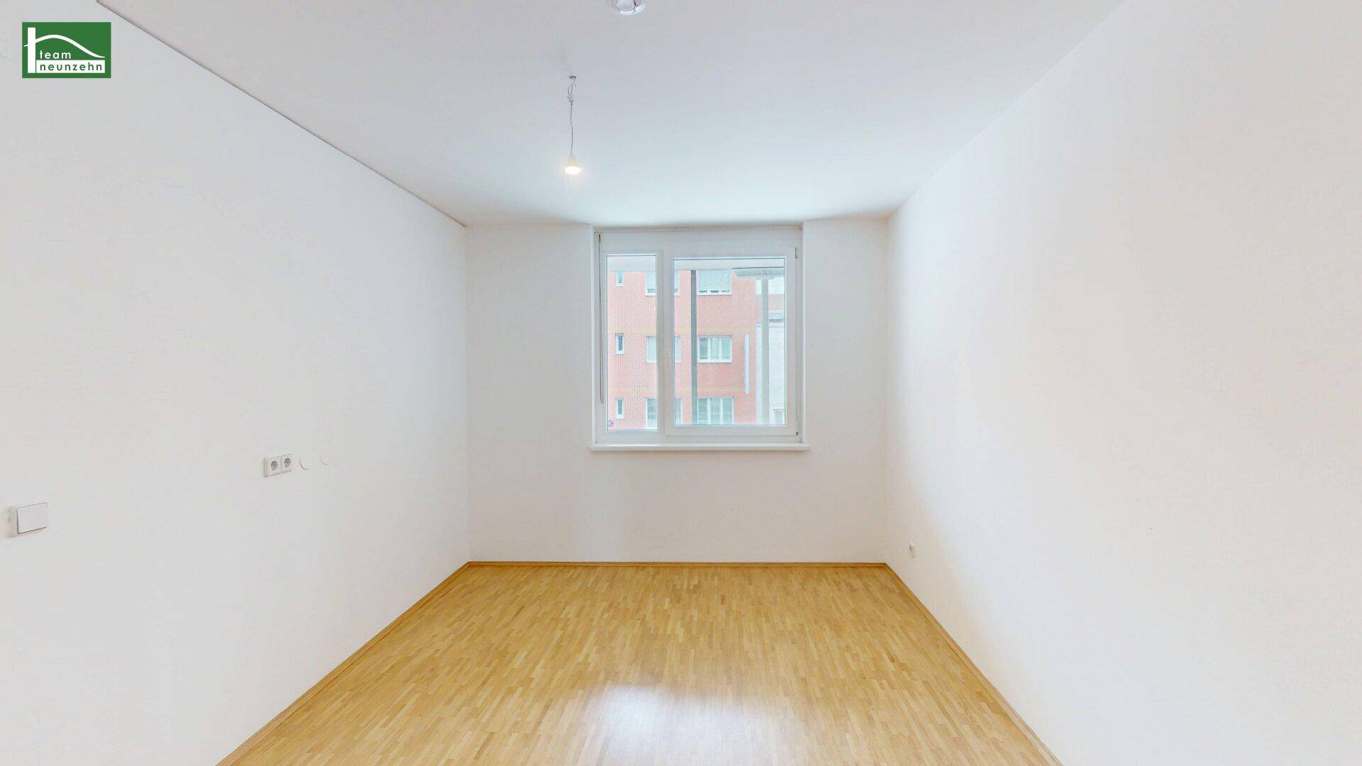 Leeres Schlafzimmer mit Parkettboden und großem Fenster, bietet viel Potenzial zur Gestaltung.