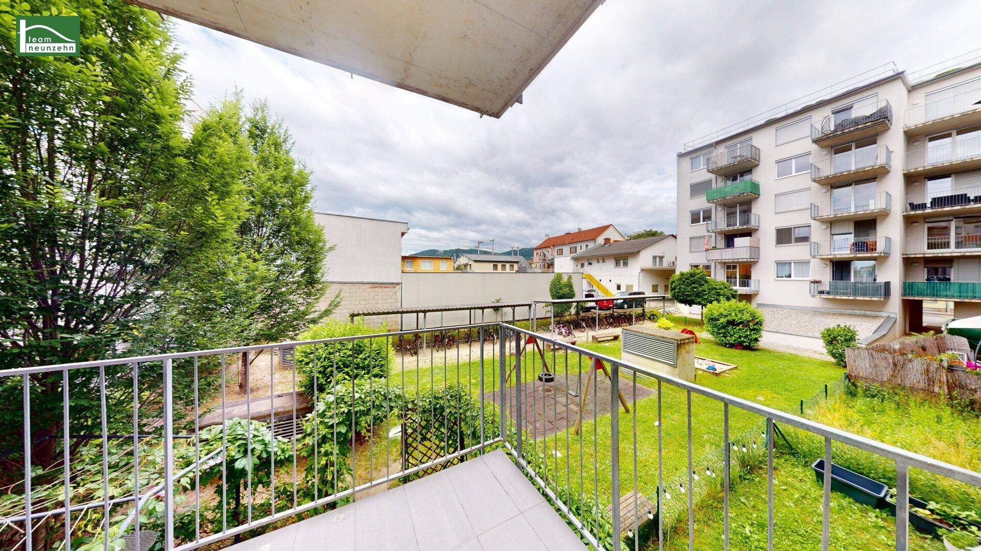 Balkon mit Blick auf einen grünen Innenhof und Kinderspielplatz.