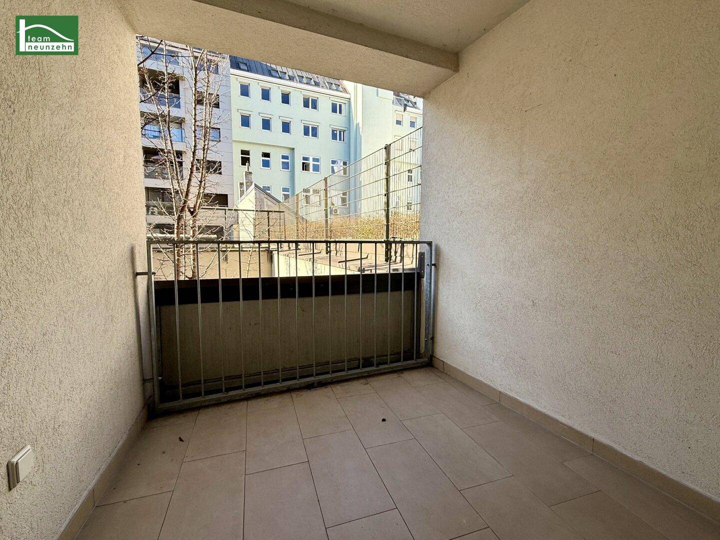 Kleiner Balkon mit Fliesenboden und Blick auf die umliegenden Stadtgebäude.
