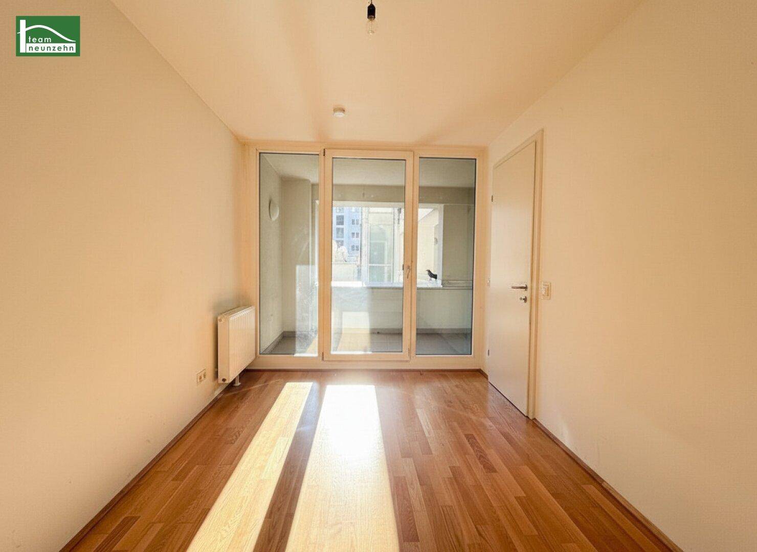 Helles Schlafzimmer mit Parkettboden und großen Fenstern, die viel Sonnenlicht hereinlassen.